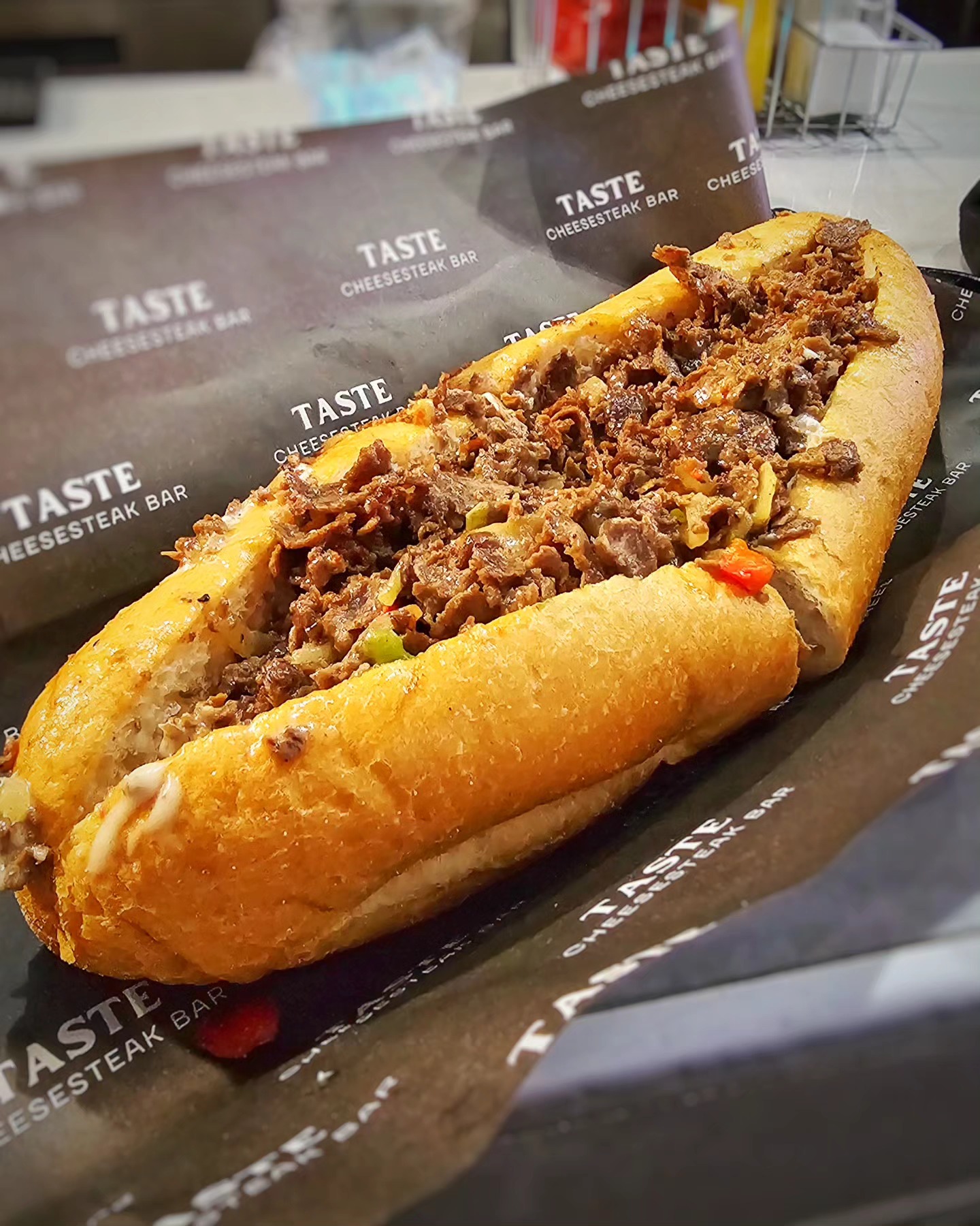 A signature Taste Cheesesteak Bar chopped beef hoagie on branded wax paper